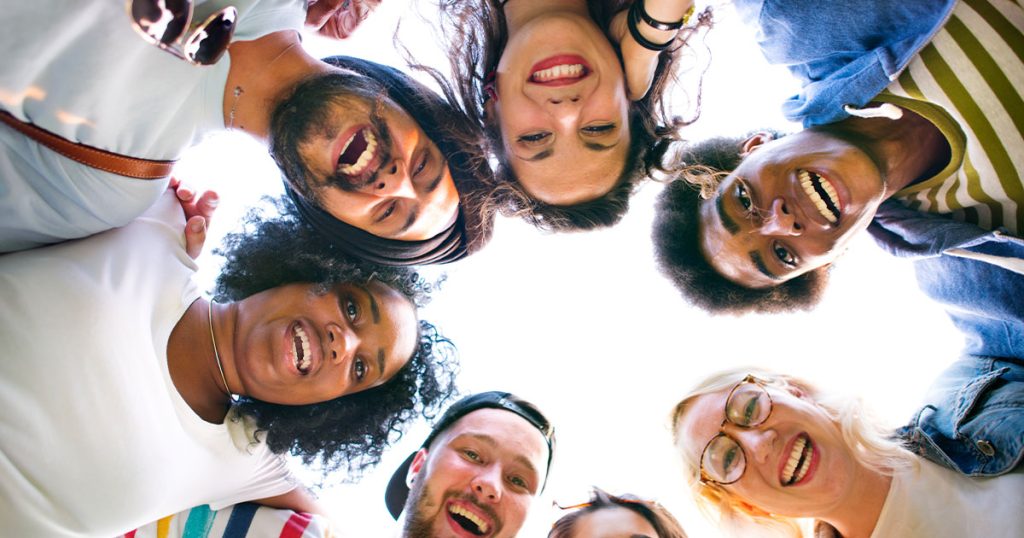Group of friends standing in a circle, smiling and looking down at the camera.