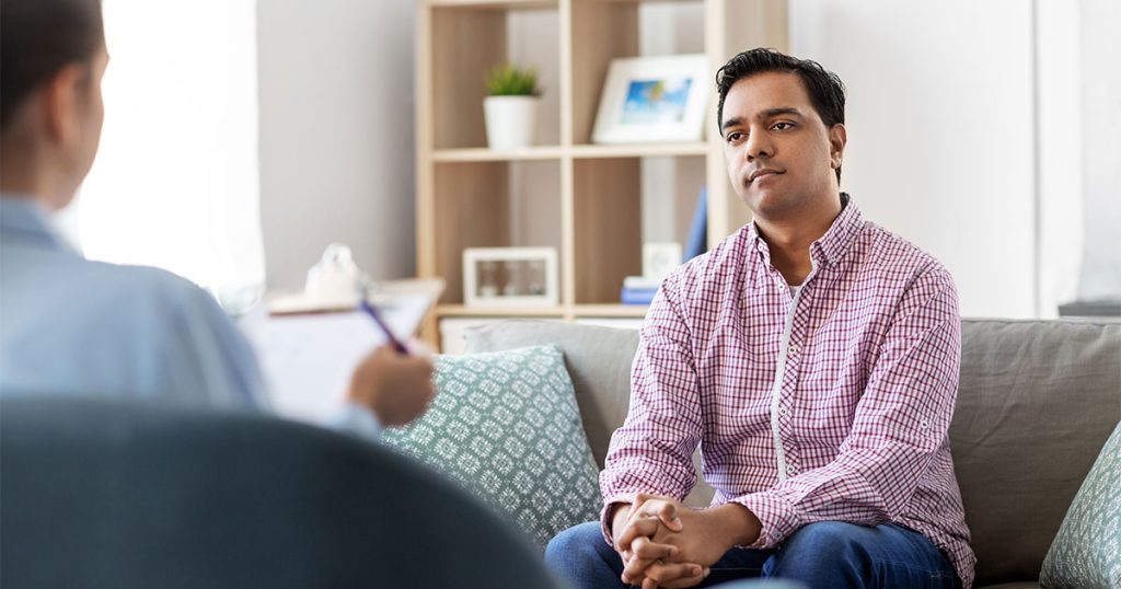 Man sitting on a couch talking to a therapist during a counseling session.